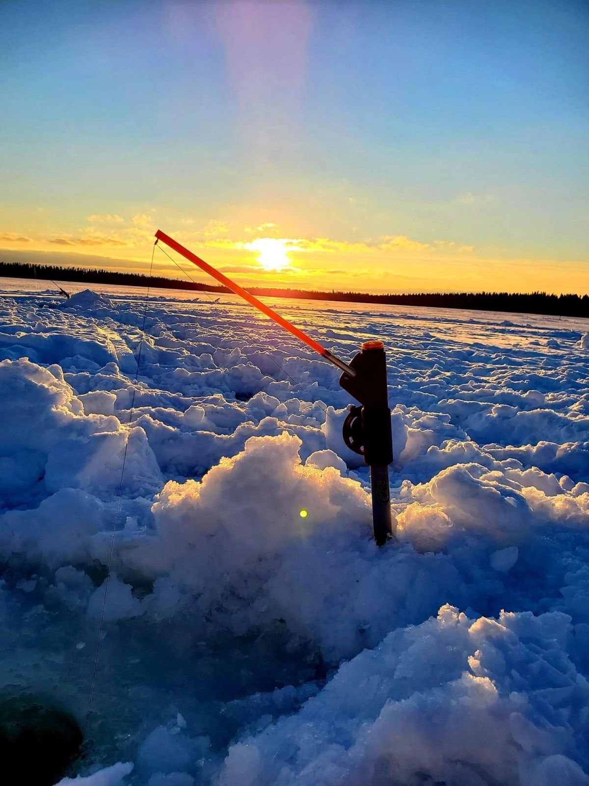 Un Chabite planté dans la neige sur un lac gelé au coucher du soleil, la tige orange tendue au-dessus du trou